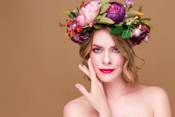schöne junge Frau Modell mit hellen Blumen auf dem Kopf auf dem ockerfarbenen Hintergrund - Foto, Bild