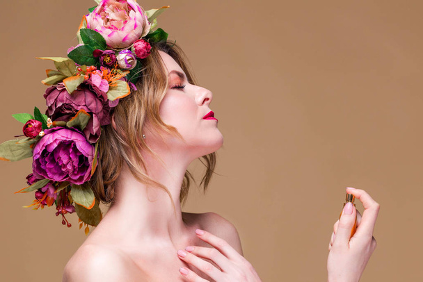 közeli kép fiatal nő virágkoszorús permetezés parfüm elszigetelt okker háttér - Fotó, kép