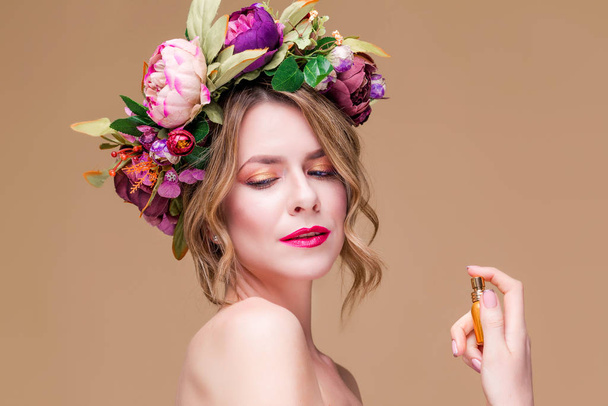 portrait en gros plan de jeune femme en couronne florale vaporisant du parfum isolé sur fond ocre
 - Photo, image