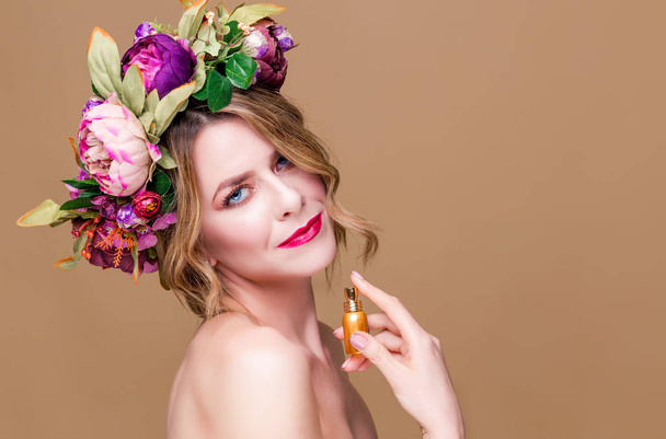 close-up portrait of young woman in floral wreath spraying perfume isolated on ocher background - Фото, изображение