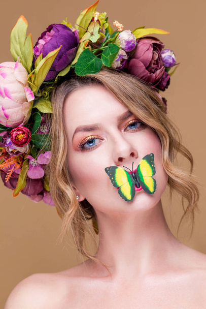 tenera giovane donna in posa in corona di fiori con farfalla verde artificiale, isolata su sfondo ochet. bocca di copertura di farfalla di una faccia di donne giovane
 - Foto, immagini