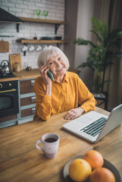 Good-looking elderly lady in yellow talking on the phone - Фото, зображення