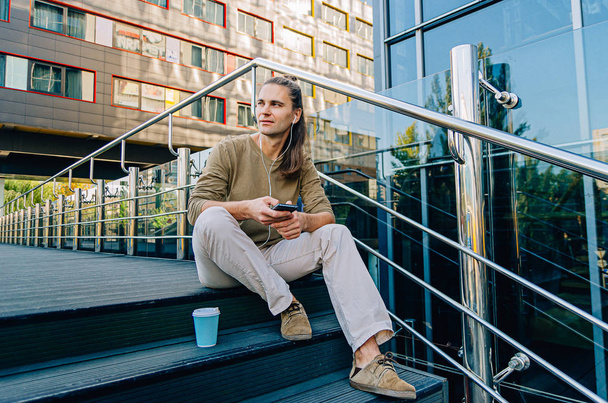 Attractive stylish hipster guy sitting on the steps of a busines - 写真・画像