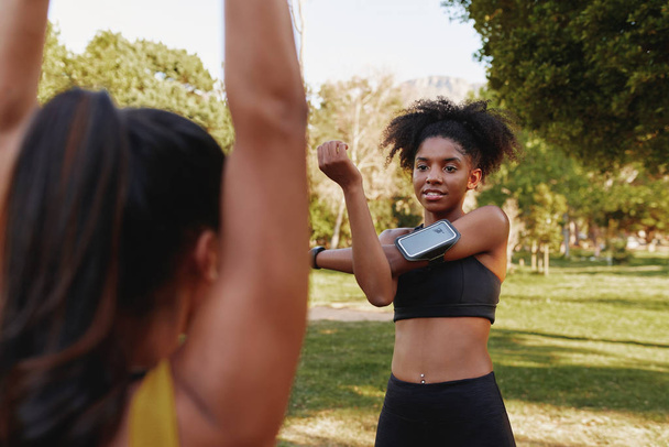 Diverse female friends standing face to face exercising together in the morning at park - fitness friends warming up their muscles together while chatting - Foto, imagen