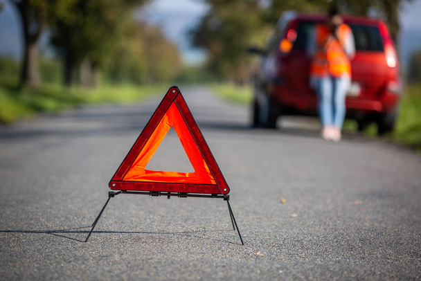Ενοχλημένη νεαρή γυναίκα σε κατάσταση οδικής κινδύνου - δημιουργία ενός προειδοποιητικού τριγώνου και έκκληση για βοήθεια - Φωτογραφία, εικόνα
