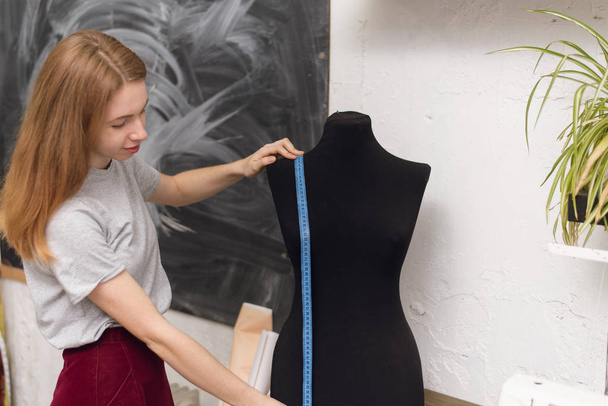 Seamstress measures on a mannequin centimeter form. Girl measures length and width on a mannequin in a sewing workshop - Fotografie, Obrázek