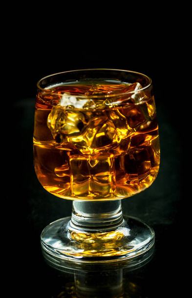 Glass with whiskey and ice cubes on a black background - Foto, Imagem