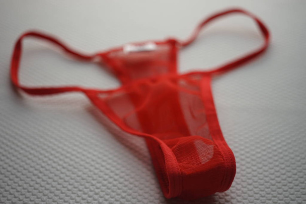 Red thong of transparent fine mesh on white fabric with embossed pattern. - 写真・画像