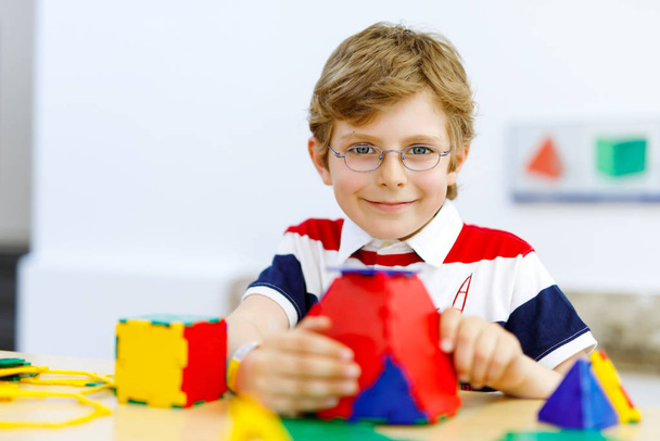Щасливий хлопчик в окулярах розважається з будівництвом і створює геометричні фігури, вивчає математику і геометрію
 - Фото, зображення