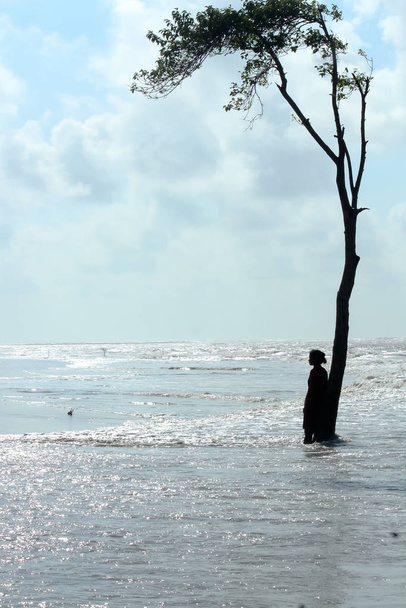 Una solitario solitario millenaria donna single in piedi lontano sotto un albero in superficie onda del mare di Blue Ocean. Giorno soleggiato isola spiaggia estiva. Turismo di viaggio Vacanze godere di concetto di sfondo di vita
. - Foto, immagini