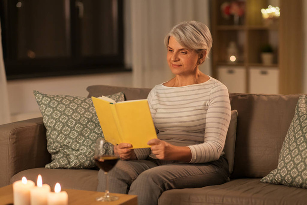 happy senior woman reading book at home in evening - Foto, imagen