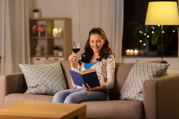young woman reading book and drinking wine at home - Foto, afbeelding