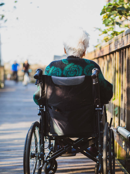 Obrázek osamělé staré ženy sedící na invalidním vozíku při pohledu na sluneční světlo. - Fotografie, Obrázek