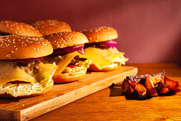 Hambúrgueres em uma tábua de madeira com batatas. Foto saborosa fast food. Lugar para texto
. - Foto, Imagem