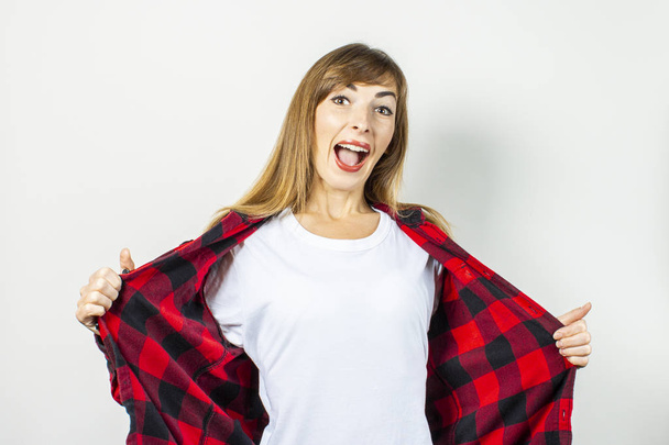 Mujer joven con una cara sorprendida en una camisa roja sobre un fondo blanco. Plantilla conceptual para texto, logo, shock, sorpresa. Banner
 - Foto, Imagen