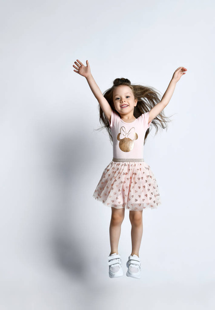 Small smiling cute girl in casual summer dress and sneakers jumping over white wall background - Fotoğraf, Görsel