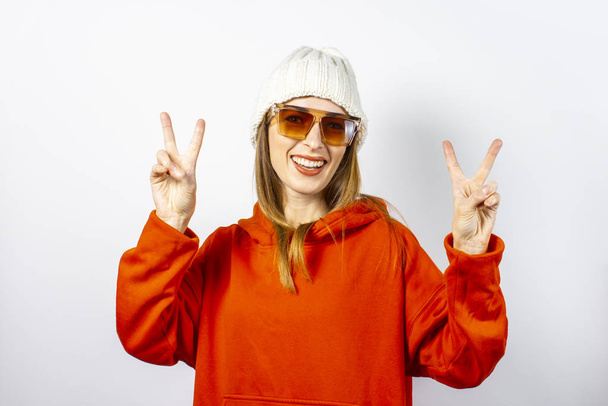 Young woman in a red hoodie, glasses and a hat on a white background. Concept modern style, youth, teens - Photo, Image