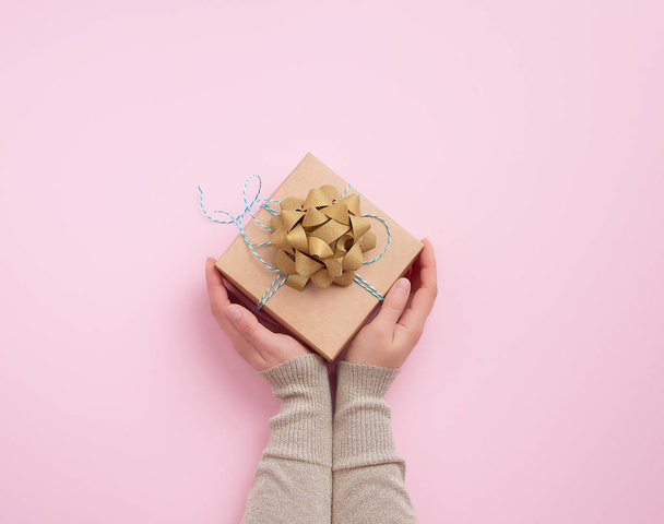 female hand holds a square box with a golden bow on a pink backg - Photo, Image
