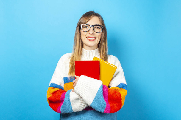 Young woman smiles and holds books in her hands on a blue background. Concept of education, college, session, exam. Banner - Photo, Image