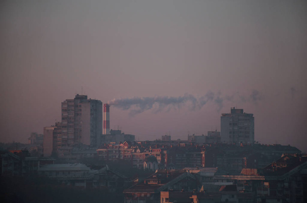 Roken uit industriële schoorstenen van verwarmingsinstallaties stoot rook uit, smog bij zonsopgang in de stad, verontreinigende stoffen komen de atmosfeer binnen. Milieuramp. Schadelijke emissies, uitlaatgassen in de lucht. Verwarmingsseizoen. - Foto, afbeelding