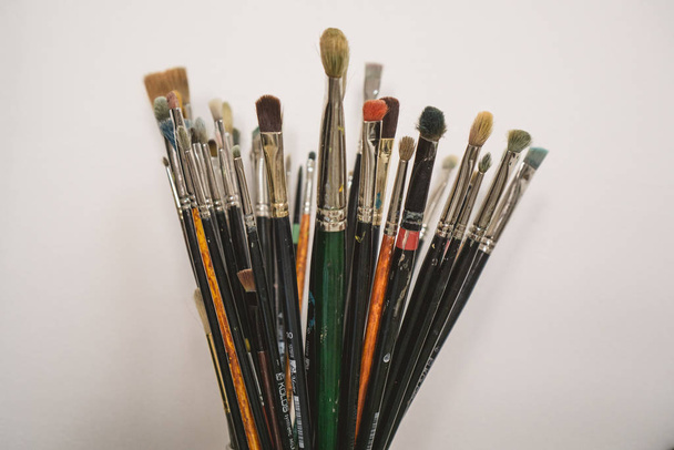Set of paint brushes. Old creativity supplies in glass on light wall background. - Photo, Image