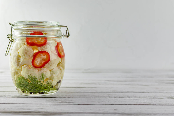 glazen pot gefermenteerde bloemkool. groenten op een lichte achtergrond. fermentatie is een bron van probiotica. kopieerruimte - Foto, afbeelding