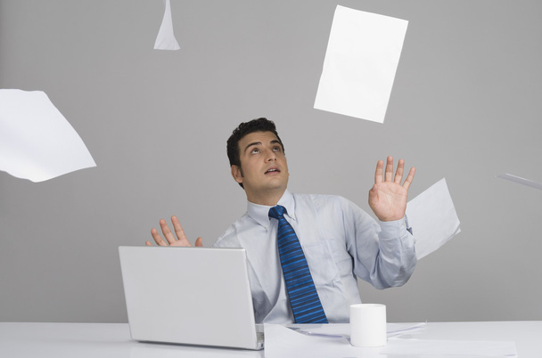 Businessman sitting in office with papers falling around him - Foto, Imagem