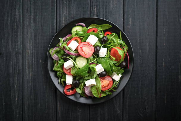 Feta, zeytin ve otlu taze sebze salatası koyu kırsal bir zeminde koyu bir tabakta. Sağlıklı vejetaryen yemeği. Üst görünüm kopyalama alanı. - Fotoğraf, Görsel