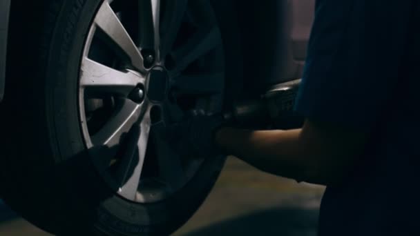 Professional car mechanic changing a car tire on lifted automobile at repair service station. Wheel alignment work at workshop night. Skillful Asian guy in uniform fixing car. 4k slow motion shot. - Footage, Video
