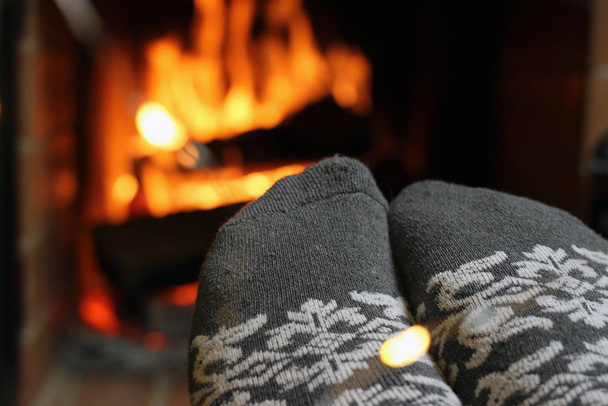 Een vrouw verwarmt haar voeten in gebreide sokken bij de open haard op een winteravond - Foto, afbeelding