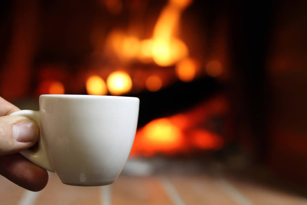 Ένα φλιτζάνι ζεστό καφέ δίπλα στο τζάκι - Φωτογραφία, εικόνα
