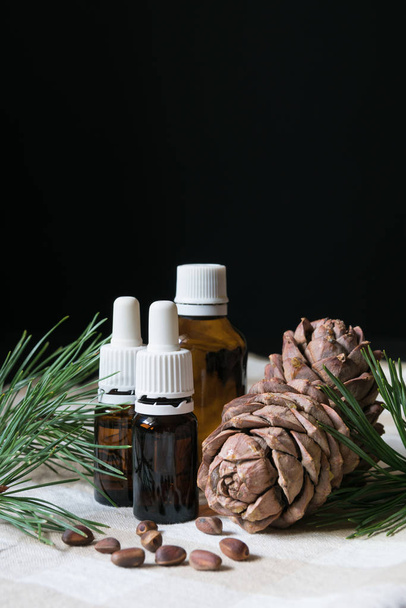 přírodní produkt, skleněné láhve s olejem, borové šišky s ořechy na ubrusu na černém pozadí, zblízka - Fotografie, Obrázek