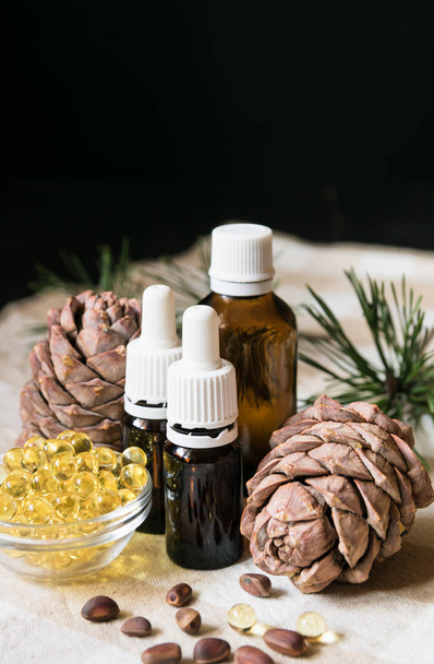 natural product, glass bottles with oil, pine cones with nuts on a tablecloth on a black background, close-up - Fotó, kép