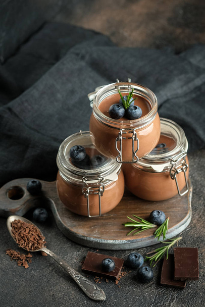 Chocolate mousse in glass jar with berries on a dark background copy space. Homemade dessert. - 写真・画像