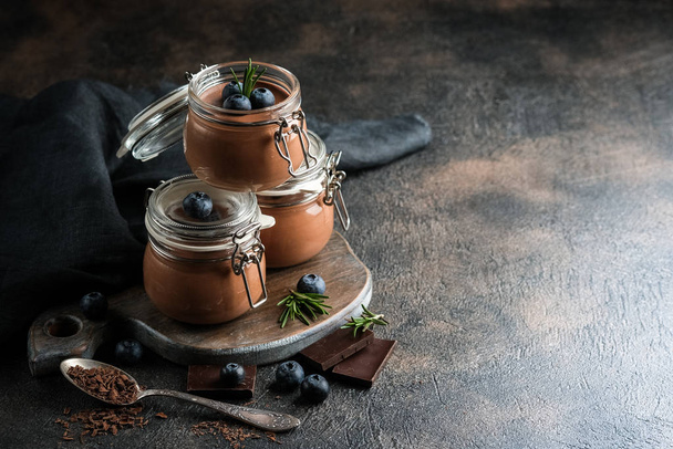 Chocolademousse in glazen pot met bessen op een donkere achtergrond kopieerruimte. Zelfgemaakt dessert. - Foto, afbeelding