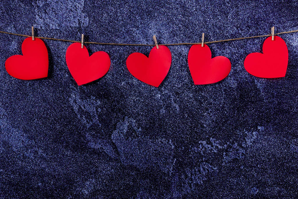 Blue classic background with a garland of red hearts. Natural rope and clothespins. Concept of recognition of love, wedding, romantic relationship, Valentines day. Copy space - Foto, Imagem