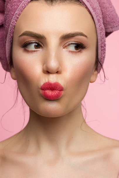 Close-up of a female portrait with a towel on her head and evening make-up. Arrows in the eyes and extremely long eyelashes. Makes a kiss on camera. Clean skin and pink lips. Thick even eyebrows - 写真・画像