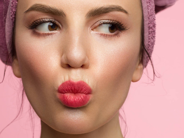 Close-up of a female portrait with a towel on her head and evening make-up. Arrows in the eyes and extremely long eyelashes. Makes a kiss on camera. Clean skin and pink lips. Thick even eyebrows - Photo, Image