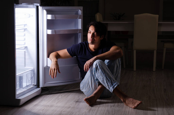 Man breaking diet at night near fridge - 写真・画像