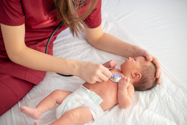 Pediatric doctor exams newborn baby girl with stethoscope in hospital - Fotó, kép