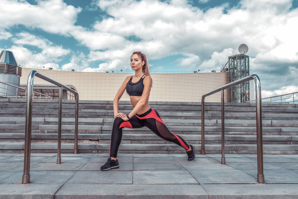 Athletic girl doing stretching before jogging, summer in city, lifestyle motivation, exercising and training on the street. Cloud stair background. Sportswear Leggings Top. - Photo, Image