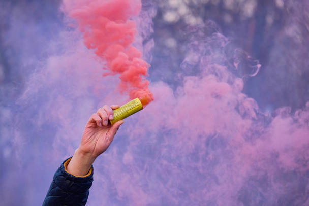 La mano sostiene un fuegos artificiales con un humo del color de rosa
. - Foto, imagen