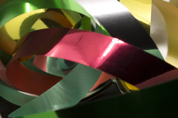 Esta es una fotografía de cintas metálicas doradas, plateadas, verdes y rojas colocadas frente a un fondo negro.
 - Foto, Imagen