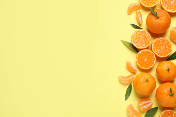 Flat lay composition with fresh ripe tangerines and leaves on light yellow background, space for text. Citrus fruit - Fotoğraf, Görsel