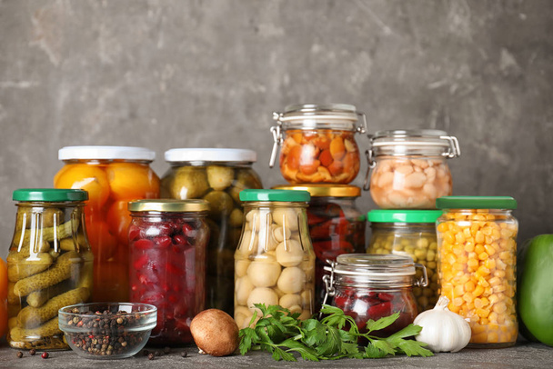 Glass jars with different pickled vegetables on grey table - Fotoğraf, Görsel