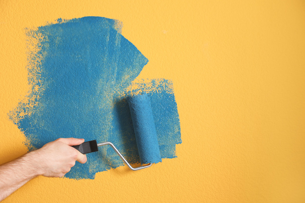 Sarı duvarı mavi boyayla boyayan adam, yakın plan. - Fotoğraf, Görsel