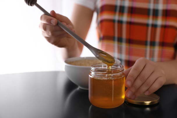 Woman with honey and spoon at black table, closeup - 写真・画像