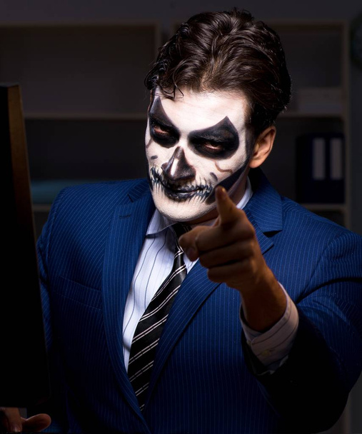 怖い顔のマスクを持つビジネスマンが遅くオフィスで働いている - 写真・画像