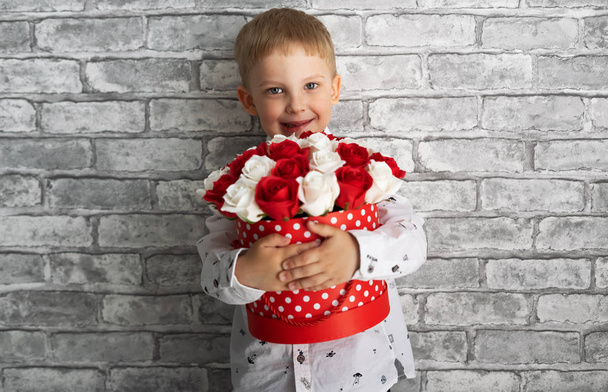 A little boy holds a big red box with red and white roses. - Foto, Imagem