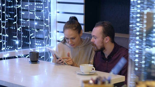 Ein Paar sitzt in einem Café, redet, trinkt Kaffee und schaut mit dem Smartphone zu.  - Filmmaterial, Video